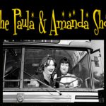 Black-and-white photo of two women (Paula and Amanda) sitting at the front of a vintage bus, smiling. Above them, bold yellow text reads “The Paula & Amanda Show” with sparkling stars.